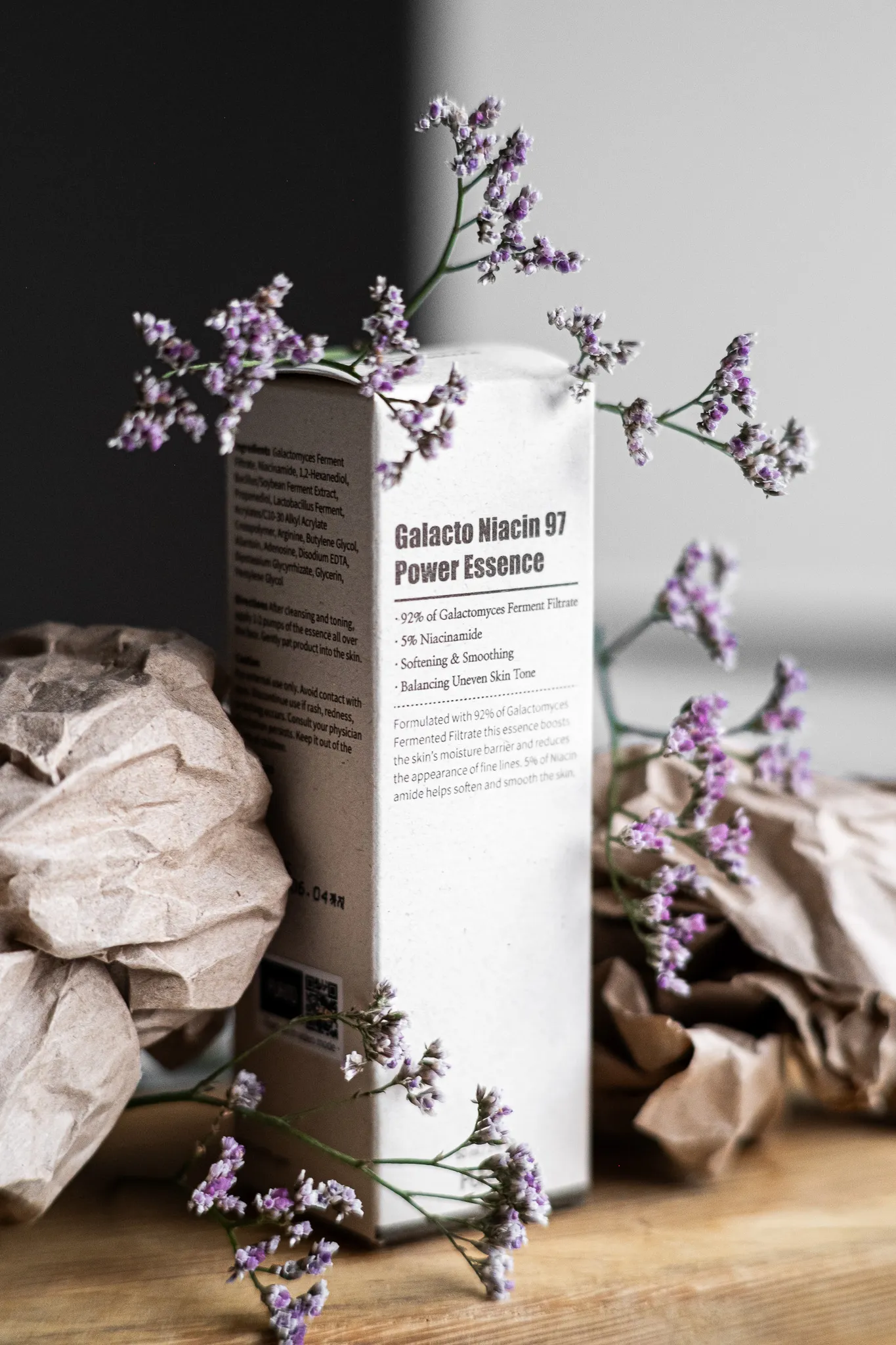 Предметна фотографія: упаковка косметичного засобу Galacto Niacin 97 Power Essence з дрібними фіолетовими квітами.