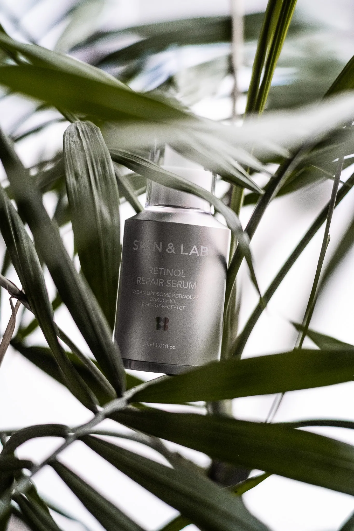 Предметна фотографія сироватки SKIN&LAB Retinol Repair Serum серед зеленого листя з природним освітленням.