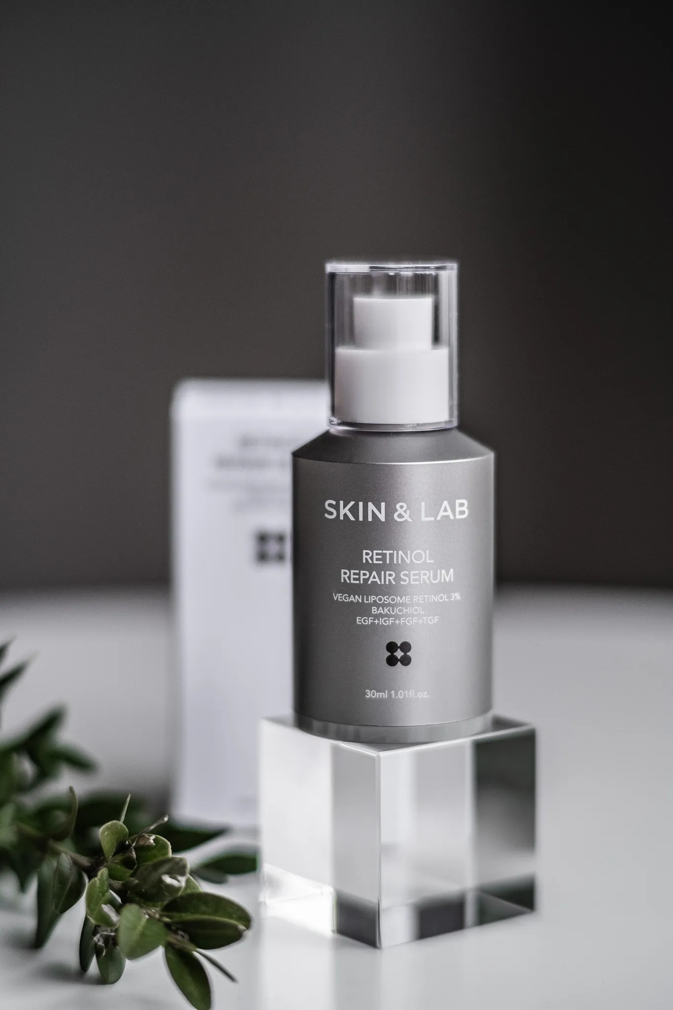 Предметна фотографія: сіра пляшка сироватки Skin & Lab Retinol Repair Serum на прозорій підставці на білому фоні.