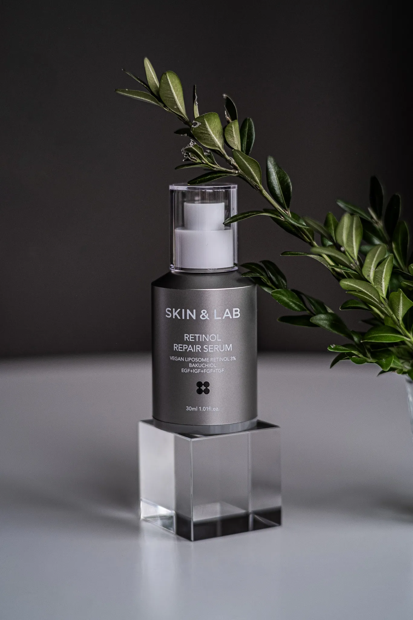 Предметна фотографія сироватки Skin & Lab Retinol Repair Serum на прозорій підставці з зеленим листям.