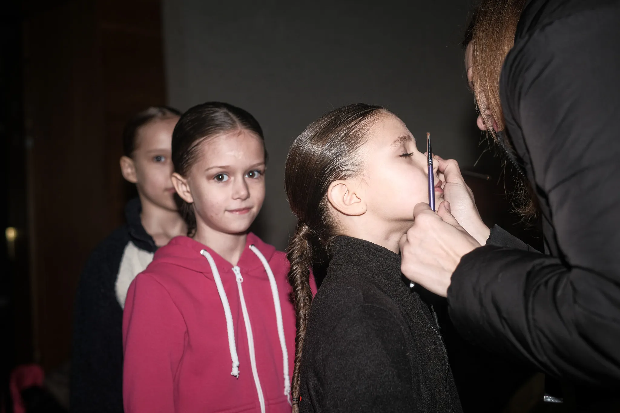 Репортаж: дівчинка наносить макіяж перед виступом, двоє дітей чекають своєї черги у заході.