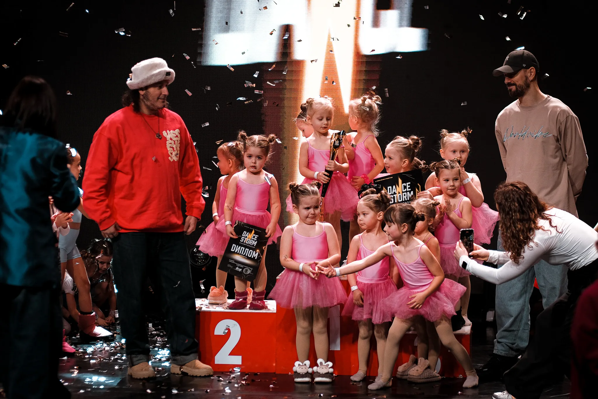 Репортаж з нагородження дітей на танцювальному конкурсі Dance Storm у рожевих костюмах та ведучі на сцені.