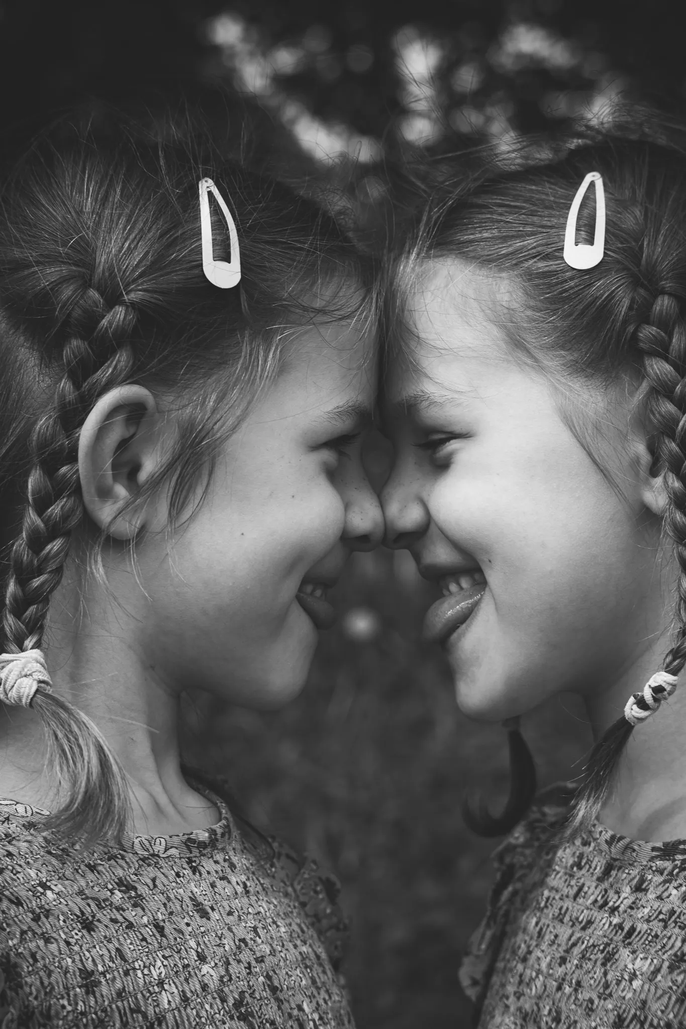 Дві усміхнені дівчинки з косами, що дивляться одна на одну, сімейна дитяча дружба, щасливе дитинство, сімейний портрет.
