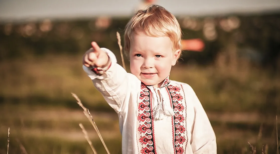 Маленька дитина в традиційному вишиваному одязі посилає руку вперед на природі. Діти, сім'я, дитинство.