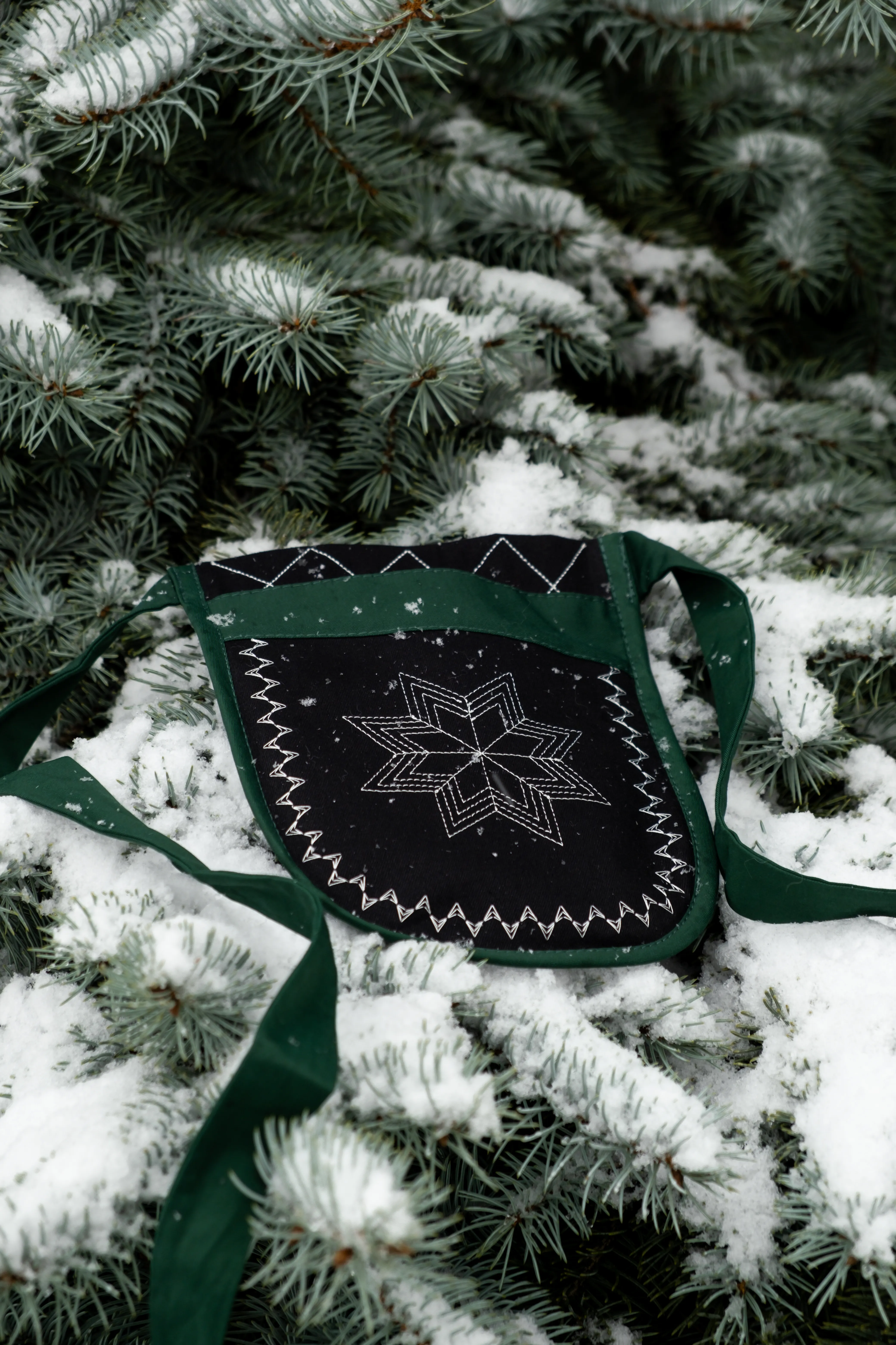 Предметна фотографія сумки з геометричним візерунком на зелених ялинових гілках зі снігом.