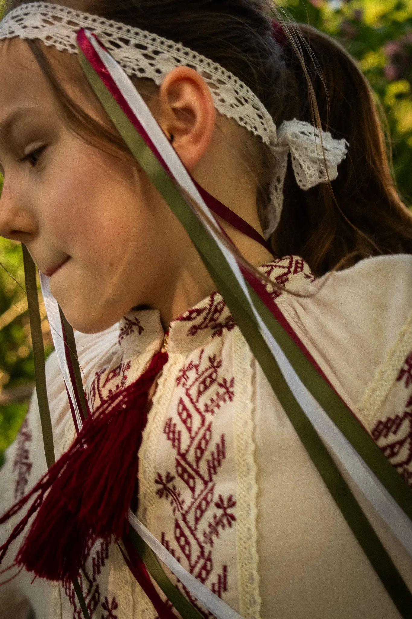Дівчина у вишиванці з мереживною стрічкою на голові під час зйомки у етностилі на природі.