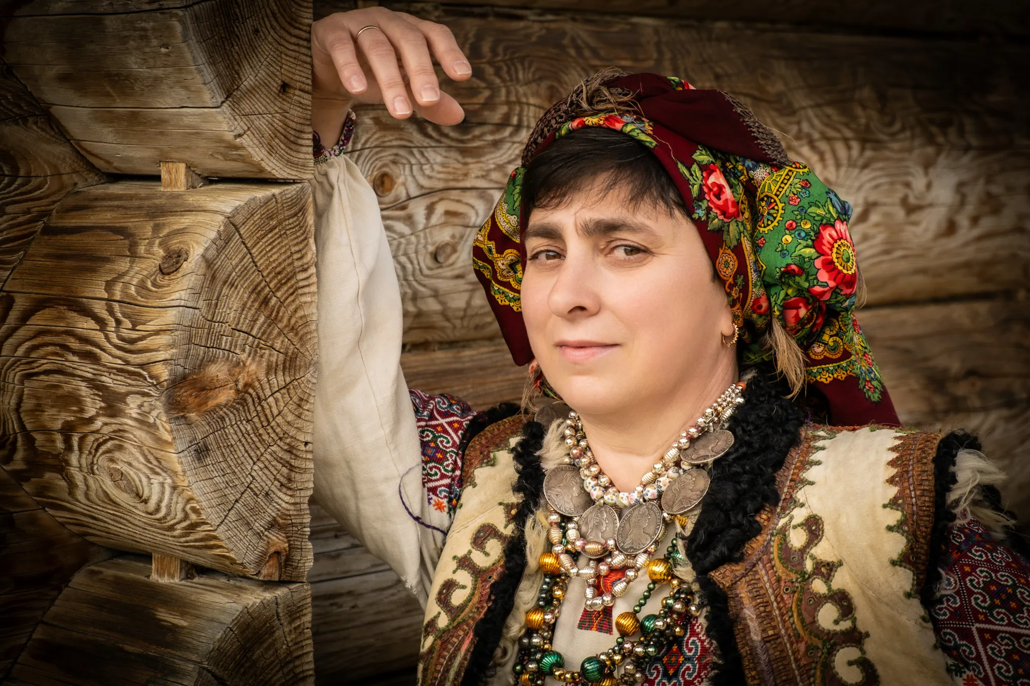Жінка в традиційному українському одязі з прикрасами біля дерев'яної хати — зйомка у етностилі.