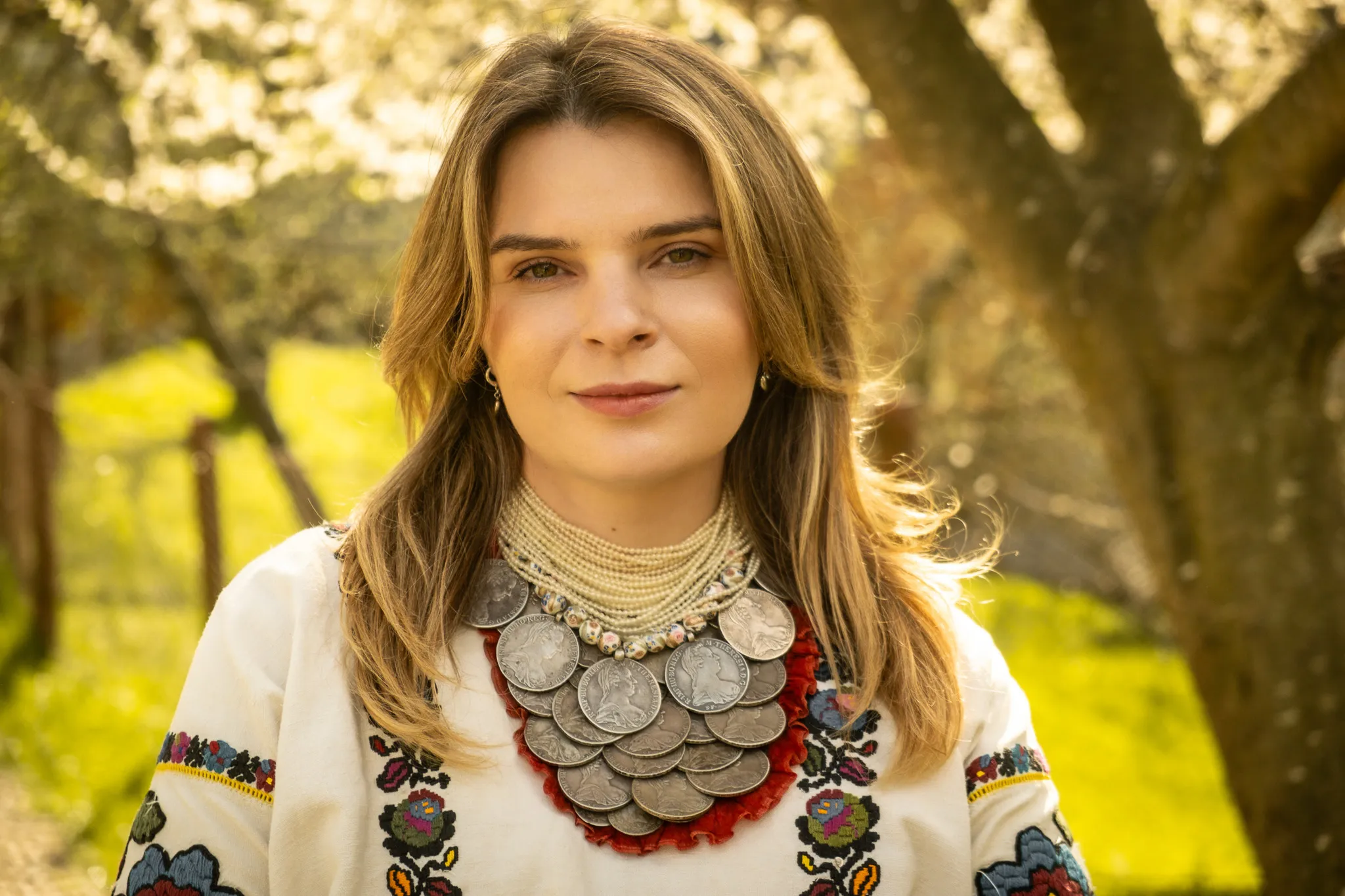 Портрет жінки у традиційному вбранні з монетним намистом, зйомка у етностилі на природі в теплий сонячний день.