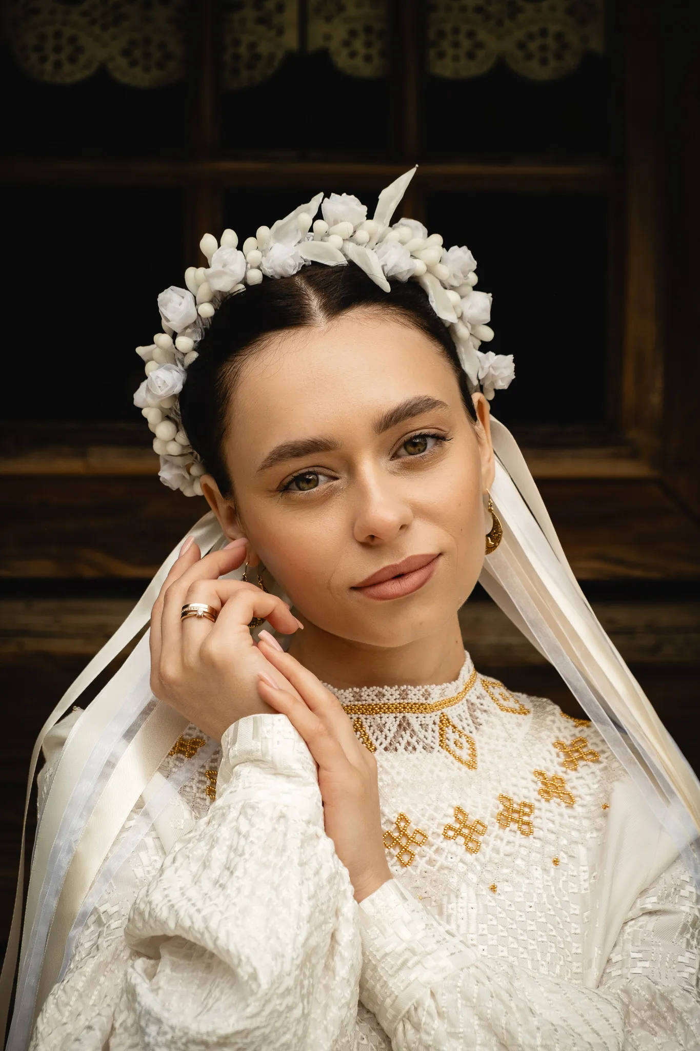 Молодята фото: молода жінка у вінку з білих квітів і традиційному вишиваному платті, портрет на темному фоні.