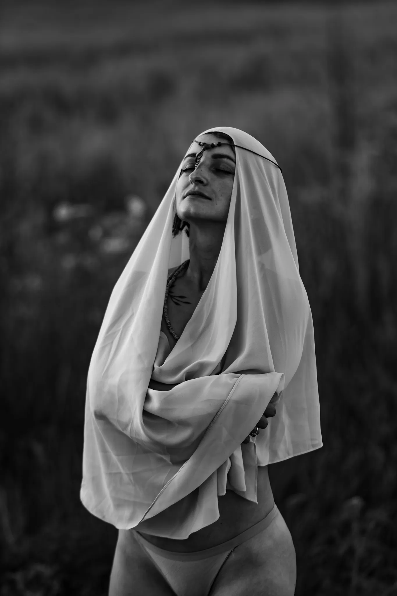 Чорно-білий портрет жінки в індивідуальній фотозйомці з серенітетним виразом обличчя, одягнена в легку тканину.